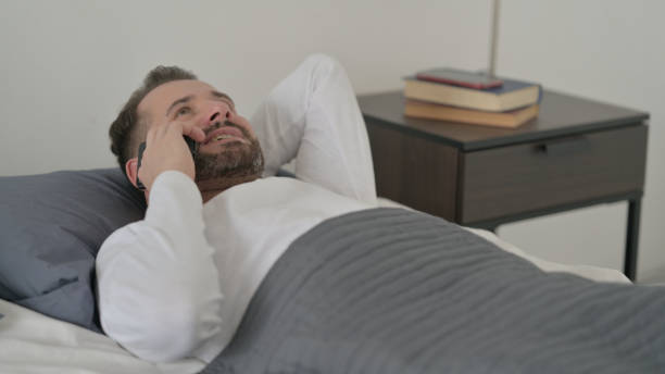 istock Man Talking on Call on Smartphone in Bed 1421631867
