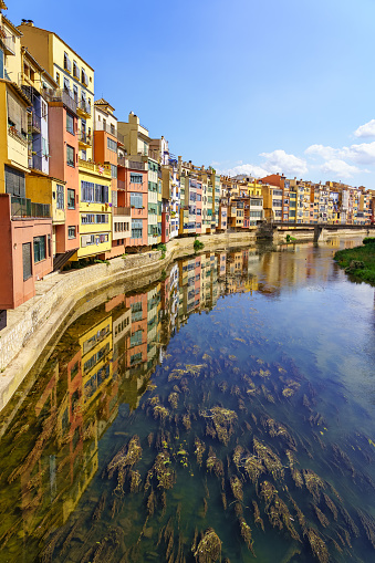 Houses of colorful colors on the banks of the river and reflection in the calm water on a sunny day, Girona, Catalonia