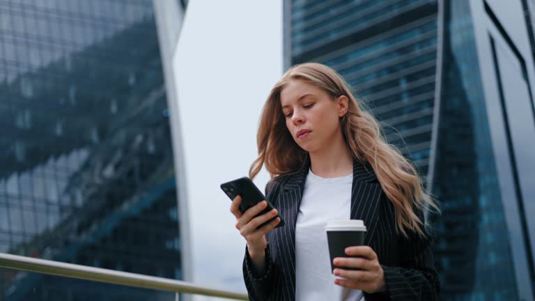 confident and emancipated businesswoman walking in big city, portrait lady with cell phone