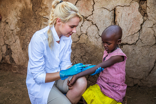 Female doctor is doing an injection to little African girl in small Masai village, Southern Kenya. Maasai tribe inhabiting southern Kenya and northern Tanzania, and they are related to the Samburu.