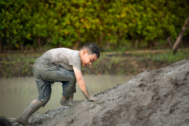 Little boys have fun playing in the mud in the community fields. with parents watching from a distance