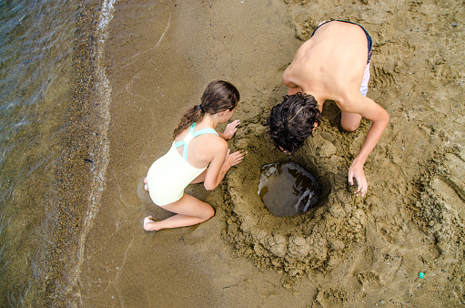 Teenage girl and boy digging a hole in sandy beach in Lake George during summer day vacations
