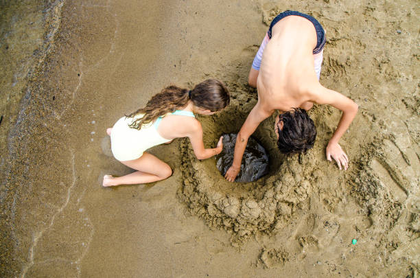 Two teenagers digging a hole in sandy beach
