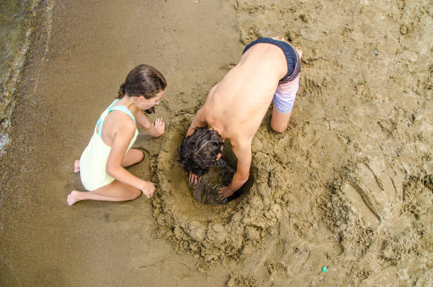 istock Two teenagers digging a hole in sandy beach 1421645369