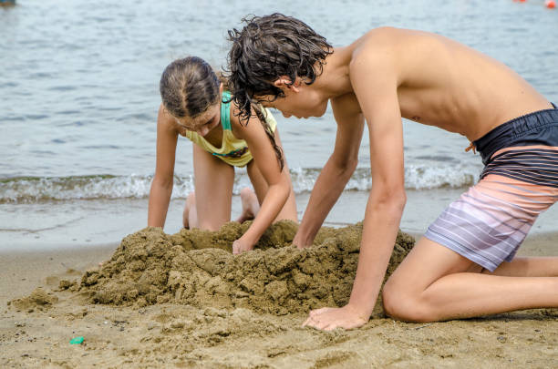 istock Two teenagers digging a hole in sandy beach 1421645426