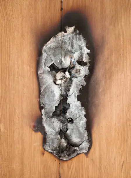 Front view of wooden apartment with peep hole and burned door decoration. Door is charred and destroyed from house fire. Selective focus.