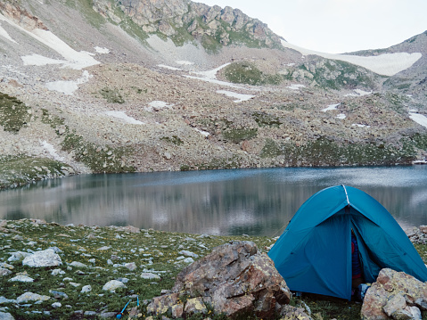 Camping tent with lake background. Mountain landscape with alone blue tent near lake on hill