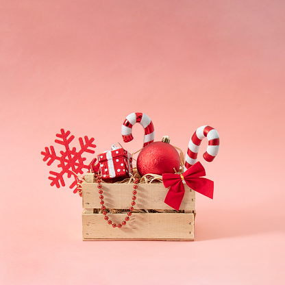 Vintage creative Christmas basket full of red decoration. Lollipop, snowflake, gift, ball and ribbon. Pink background.
