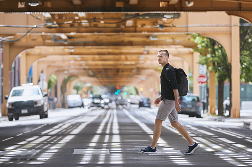 Man with backpack walking on pedestrian crosswalk uder elevated railway