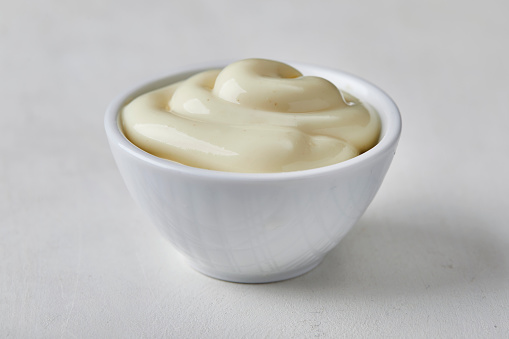 Mayonnaise in a small ceramic bowl, on a white wooden cutting board, top view with a space for copy