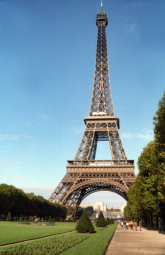 Paris, France - 1983: A vintage 1980's Fujifilm negative film scan of the Eiffel tower in Paris, France across the lush Champs de Mars public park on a clear blue sky day.