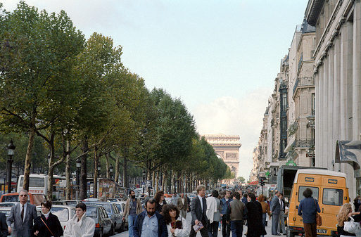 Paris, France - 1983: A vintage 1980's Fujifilm negative film scan of the sidewalks down the  down the  avenue des Champs Elysees with crowds of tourists and the Arc de Triomphe in the background.