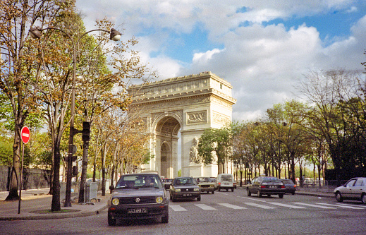 Paris, France - 1983: A vintage 1980's Fujifilm negative film scan of the Arc de Triomphe in Paris during a light golden sunrise morning with light car traffic.