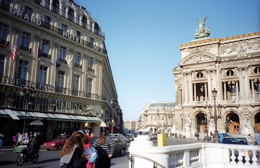 Paris, France - 1983: A vintage 1980's Fujifilm negative film scan of the intersection and metro entrance in front of the Palais Garnier Paris opera house and Le Grand Hotel with vintage cars driving across the street.