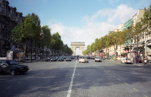 Paris, France - 1983: A vintage 1980's Fujifilm negative film scan of the Arc de Triomphe as seen down the  avenue des Champs Elysees with crowds of people and of cars in the street.