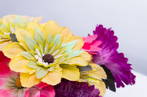 Close up to a yellow plastic flower on an isolated white background. Flowers of many colors pink, purple and yellow.