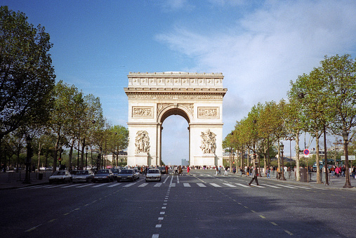 Paris, France - 1983: A vintage 1980's Fujifilm negative film scan of tourists in front of and under the the Arc de Triomphe in Paris, France on a bright clear blue sky day.