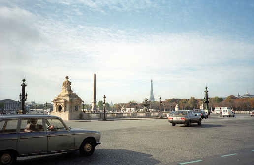 Paris, France - 1983: A vintage 1980's Fujifilm negative film scan of morning rush hour streets in central Paris, France with cars and pedestrians traveling.