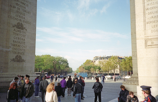 Paris, France - 1983: A vintage 1980's Fujifilm negative film scan of tourists in front of and under the the Arc de Triomphe in Paris, France on a bright clear blue sky day.