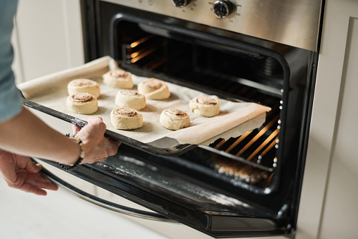 Close-up of young woman baking sweet buns in oven at home