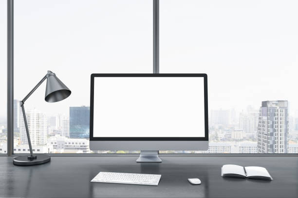 istock Close up of blank white computer screen on gray office desktop with objects, lamp and supplies on panoramic window and city view background. Mock up, 3D Rendering. 1421663997