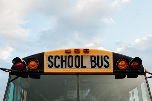 Front top view of a yellow school bus on a sky with clouds. High quality photo
