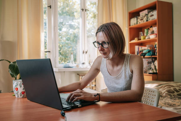 istock Young woman sitting by window, working, studying or surfing with laptop. 1421666446
