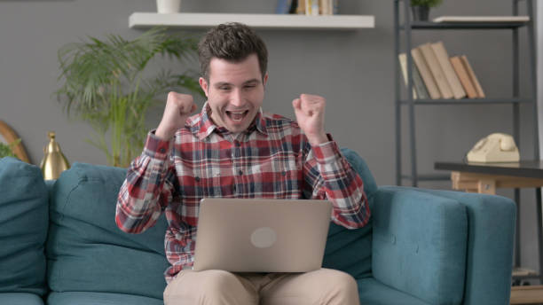 istock Man with Laptop Celebrating Success on Sofa 1421670357