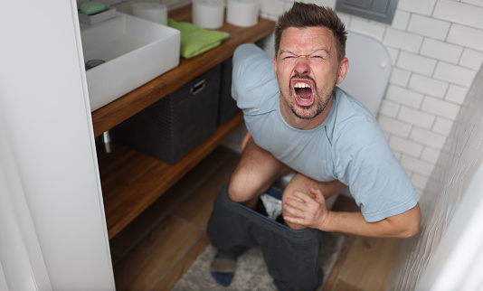 Hombre que sufre de hemorroides grita en el inodoro en el inodoro photo