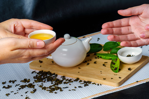 Hands pass each other a small bowl of green tea