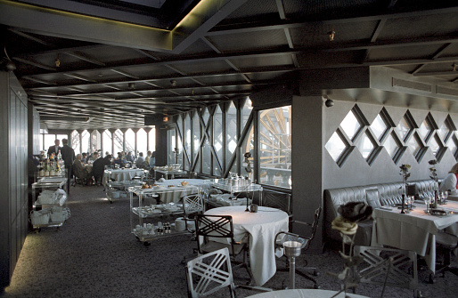 Paris, France - 1983: A vintage dark 1980's Fujifilm negative film scan of the interior of the former restaurant that was located in the top of the Eiffel tower in Paris, France with customers dining.