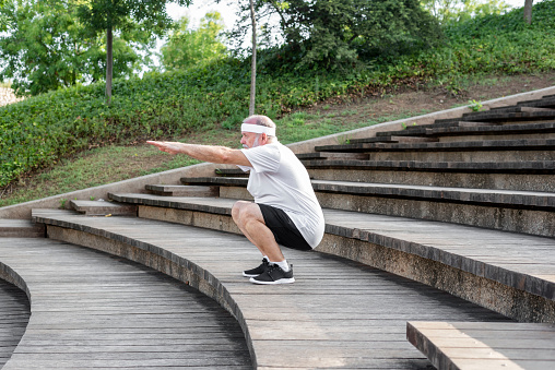 Healthy lifestyle for retirement. Older mature man during outdoor workout, senior man warming up muscles, doing squats on the stairs