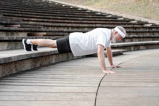 Elderly male retiree is doing push ups exercise outdoor. Stay active in retirement