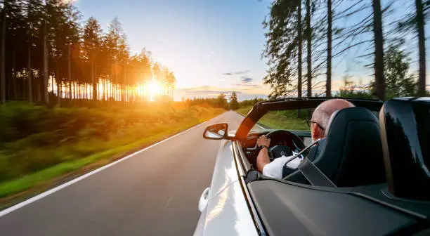 Mature Adult man is driving with convertable car in sunny nature on a bright summer day. wide angle pursuit shot with high speed motion blur.