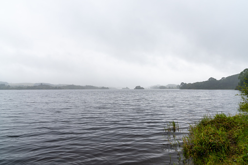 Landscape view of misty and foggy atmosphere over a calm lake surrounded by lush green forest