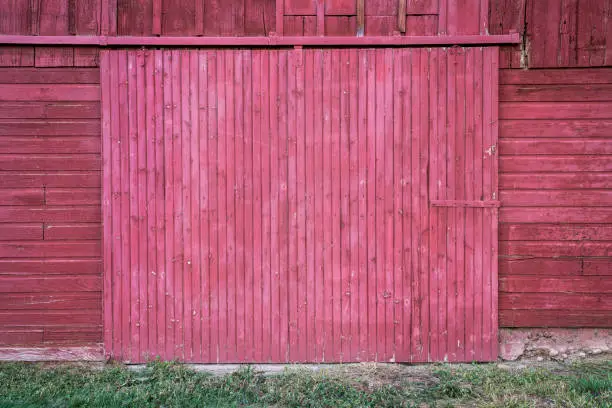 wall of old, wooden, weathered red painted barn with a sliding gate - rustic wood background and texture