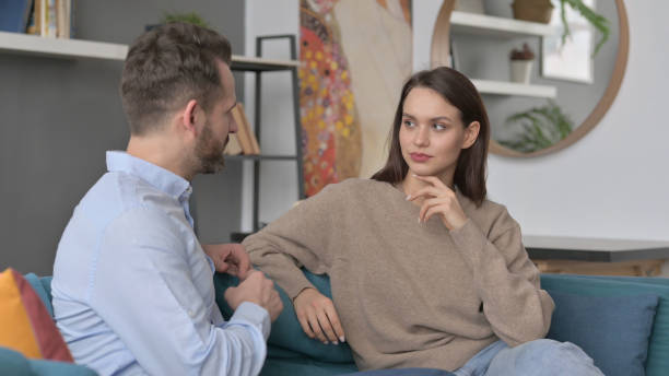 istock Man Talking to Woman while Sitting on Sofa 1421684472