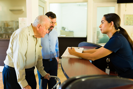 Hispanic nurse giving admission information about the retirement home to a mature old man using a walker at the nursery home