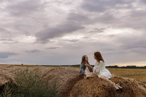 Mom in a white dress and daughter are sitting on haystacks
