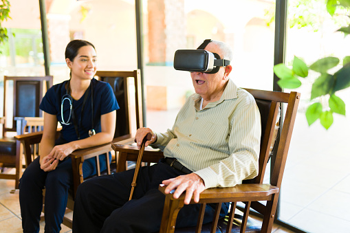 Excited old man in his 80s looking happy and having fun at the nursery home while playing with virtual reality glasses