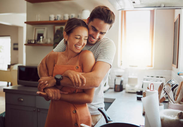 love, romance and fun couple hugging, cooking in a kitchen and sharing an intimate moment. romantic boyfriend and girlfriend embracing, enjoying their relationship and being carefree together - pojkvän bildbanksfoton och bilder