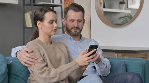 istock Portrait of Couple using Smartphone While Sitting on Sofa 1421688597