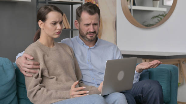 istock Couple Reacting to Loss on Laptop while Sitting on Sofa 1421691818