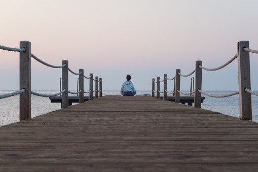 Woman meditating alone on the pier at sunrise. Sense of calm, peace, balance, healing and a healthy lifestyle concept.