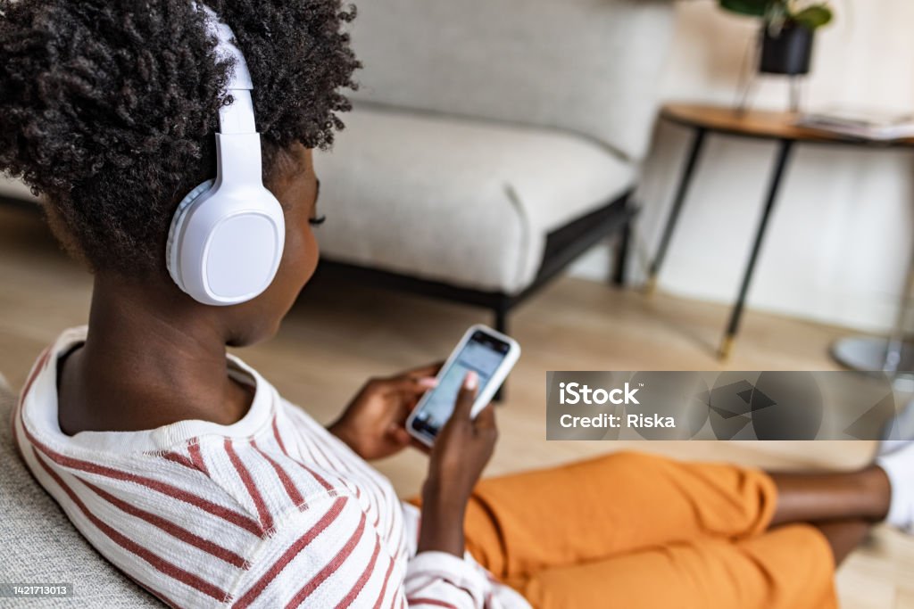Young woman surfing the net on the smart phone Young woman sitting on the floor, using mobile phone and listening music via wireless headphones connected to her smart phone One Person Stock Photo
