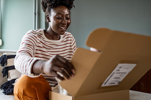 Young excited woman unpacking parcel at home after shopping online