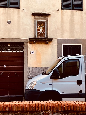 White van parked outside classic tuscan town house , 7th September 2022 in Lucca. Lucca is a city on the Serchio river in Italy’s Tuscany region. It’s known for the well-preserved Renaissance walls encircling its historic city center and its cobblestone streets. Broad, tree-lined pathways along the tops of these massive 16th- and 17th-century ramparts are popular for strolling and cycling. Casa di Puccini, where the great opera composer was born, is now a house museum.