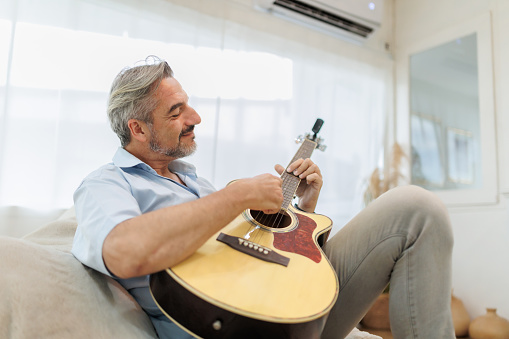 Mature Adult Man playing acoustic guitar in the living room.