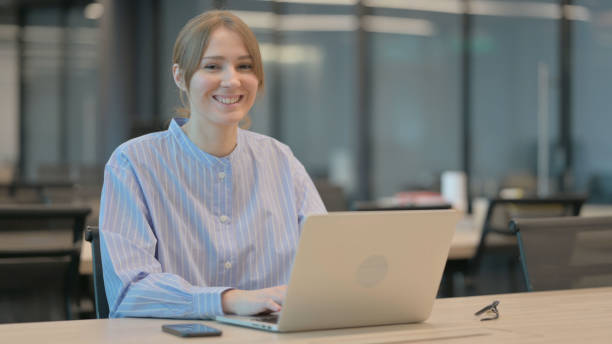 istock Young Woman Smiling at Camera while using Laptop in Office 1421725346