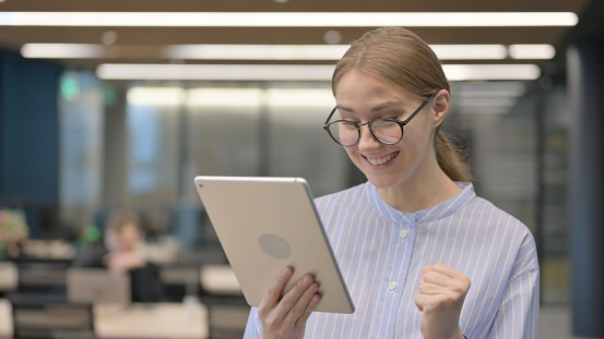 Portrait of Casual Young Woman Celebrating on Tablet in Office